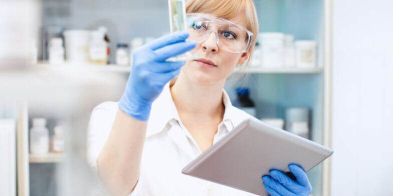 Scientist Looking at Measuring Cylinder, Holding a Tablet