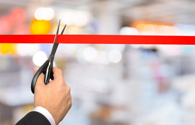 Businessman cutting red ribbon with pair of scissors