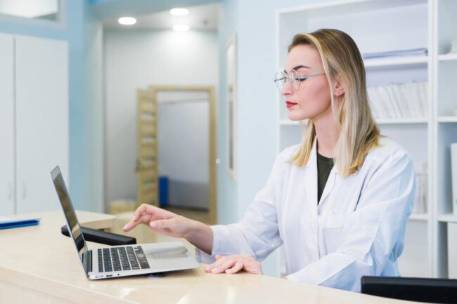 Smiling nurse with laptop scheduling appointment for male patient at reception.
