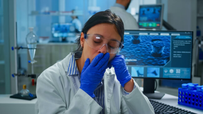 Outbreak chemist looking tired at camera, yawning working in lab